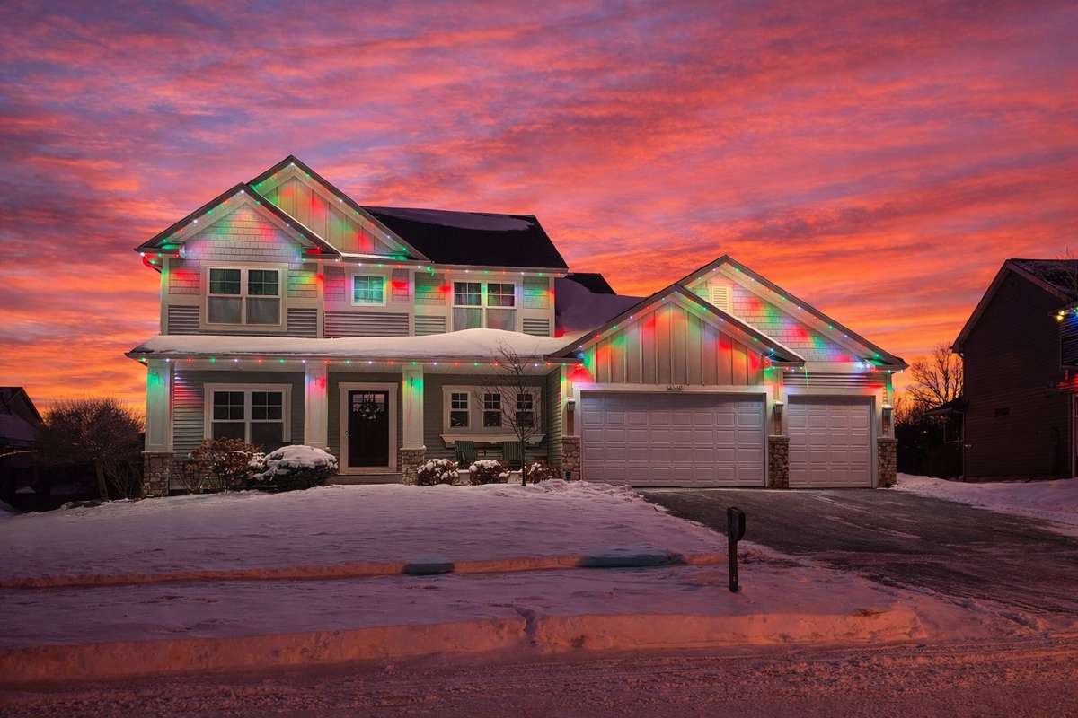 Christmas red and green lights on two-story home at fiery sunset